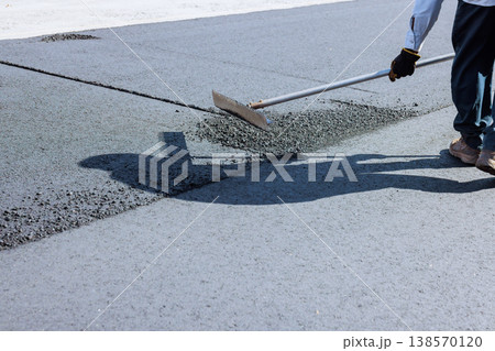 Builder uses rake to spread hot asphalt on ground at construction site during road works Builder uses rake to spread hot asphalt on ground at construction site during road works 138570120