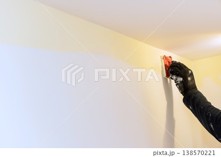 Carpenter using tool to smooth paint on wall in home wall shows two colors of paint. Carpenter using tool to smooth paint on wall in home wall shows two colors of paint. 138570221