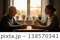 Adult daughter sitting with her elderly father at a table drinking tea by a window with warm sunset light. Calm atmosphere. Concept of care and family connection. 138570341