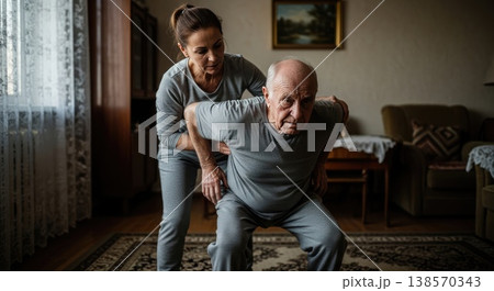 Adult daughter helping her elderly father perform light physical exercises at home. Daily care routine and support. Concept of rehabilitation and senior health. 138570343