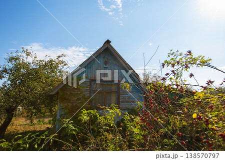 A small wooden village country house with a triangular roof. An old hut with a garden plot. A small wooden village country house with a triangular roof. An old hut with a garden plot. 138570797