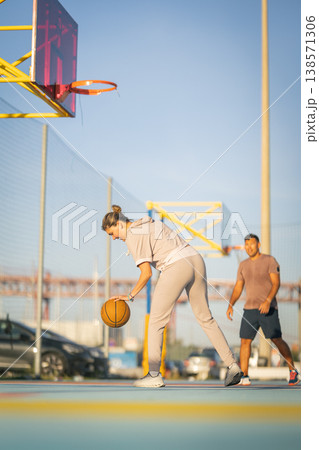 Woman dribbling basketball on multisport court with man watching Woman dribbling basketball on multisport court with man watching 138571306