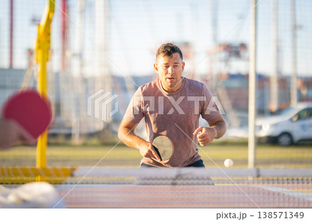 Focused man playing outdoor table tennis match at sunset Focused man playing outdoor table tennis match at sunset 138571349