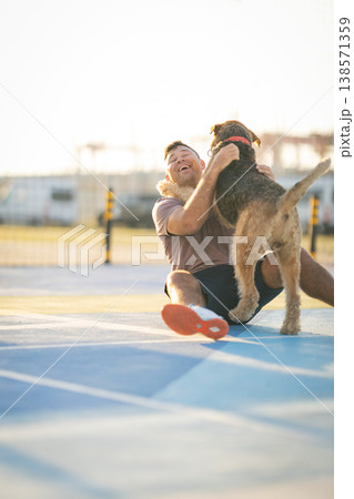 Happy man laughing hugging dog on colorful outdoor court Happy man laughing hugging dog on colorful outdoor court 138571359