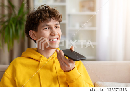 Young smiling teen guy in yellow hoodie holding phone in speakerphone mode Young smiling teen guy in yellow hoodie holding phone in speakerphone mode 138571518