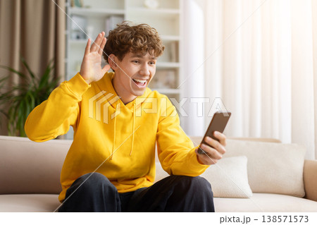 Excited teen guy waving hand at smartphone screen during video call 138571573