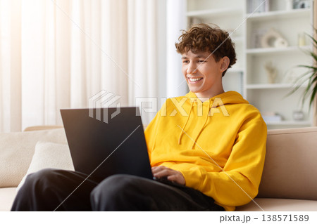 Happy young teen sitting on sofa with laptop, smiling and looking away Happy young teen sitting on sofa with laptop, smiling and looking away 138571589