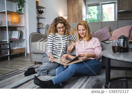 Two female friends looking at an old photo album at home Two female friends looking at an old photo album at home 138572117
