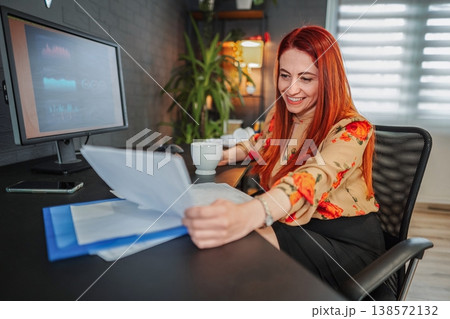 Businesswoman smiling while reading documents at her desk 138572132