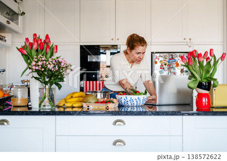 Mature woman searching recipe online on laptop while cooking in kitchen. 138572622