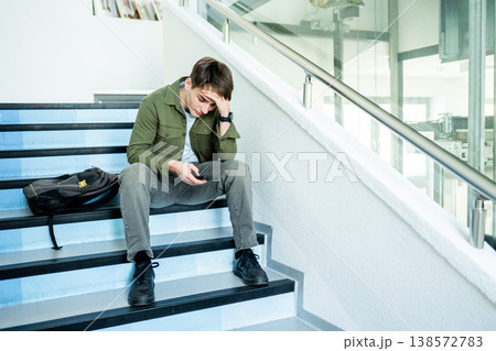 Depressed male student sitting on stairs and looking at phone. 138572783