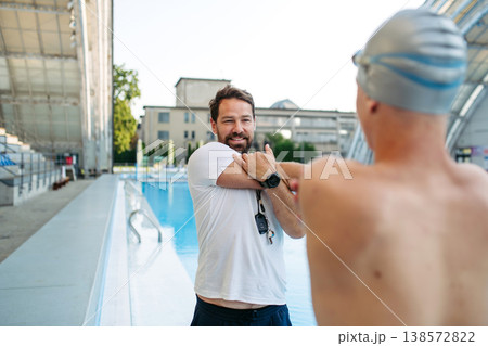 Coach preparing young swimmer for competition, stretching arms. 138572822