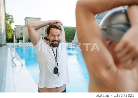 Coach preparing young swimmer for competition, stretching arms. 138572823