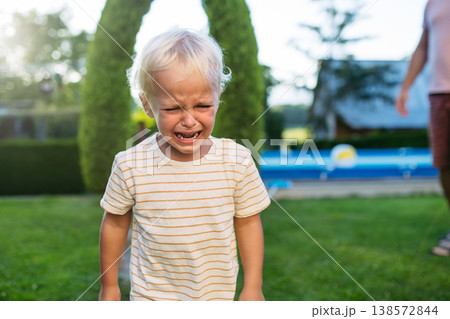 Crying toddler boy standing in garden with strong emotion. Crying toddler boy standing in garden with strong emotion. 138572844