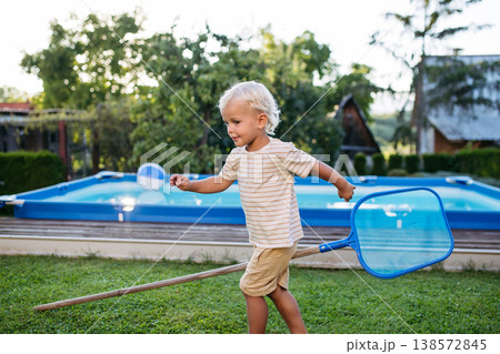 Smiling blond child playing in garden during warm summer day. Smiling blond child playing in garden during warm summer day. 138572845