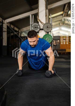 Man performing push-ups with dumbbells at gym Man performing push-ups with dumbbells at gym 138572974