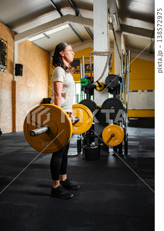 Woman standing with barbell after lifting weights 138572975