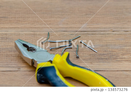 Pliers and bent nails on wooden surface showing repair process and damage Pliers and bent nails on wooden surface showing repair process and damage 138573276