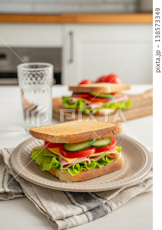 Two club sandwiches with ham, cheese, tomatoes, lettuce, cucumber on a plate on a kitchen table 138573349