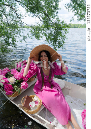 An elegant woman poses gracefully in a stunning red dress with floral arrangement against a calm water backdrop An elegant woman poses gracefully in a stunning red dress with floral arrangement against a calm water backdrop 138573726