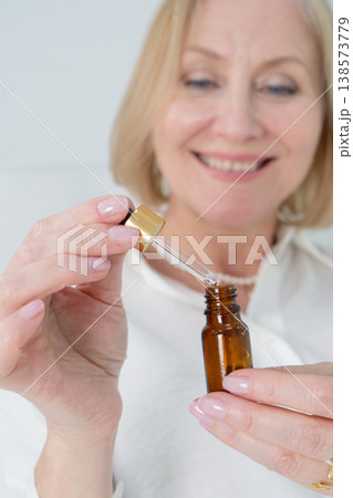 A woman is gracefully holding an essential oil bottle with a dropper in a beautifully elegant, serene setting A woman is gracefully holding an essential oil bottle with a dropper in a beautifully elegant, serene setting 138573779