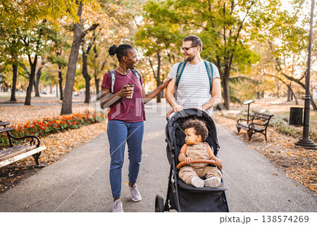 Mixed race couple walks their son's stroller through the park Mixed race couple walks their son's stroller through the park 138574269