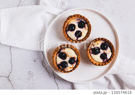 Close up baked mini tartlets with cottage cheese and black currant on a plate on the table top view Close up baked mini tartlets with cottage cheese and black currant on a plate on the table top view 138574618