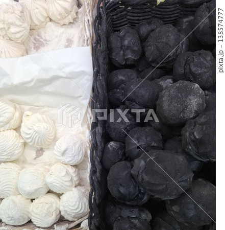 In a basket, there are white marshmallows and black marshmallows next to each other. Many people gather around to look at the unique shapes and colors during a busy market. In a basket, there are white marshmallows and black marshmallows next to each other. Many people gather around to look at the unique shapes and colors during a busy market. 138574777