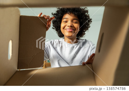 Inside of cardbox bottom view. African girl unpacking delivery looking in box. Woman opening carton box. Female getting parcel looking at delivered goods items. Satisfied client positive feedback Inside of cardbox bottom view. African girl unpacking delivery looking in box. Woman opening carton box. Female getting parcel looking at delivered goods items. Satisfied client positive feedback 138574786