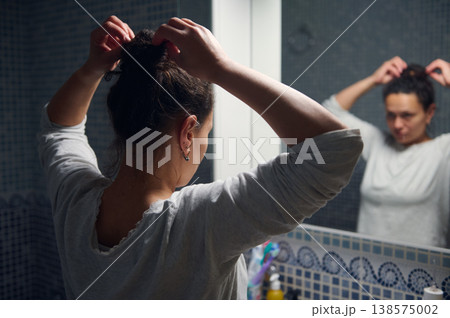 Middle-Aged Woman Doing Morning Beauty Routine in Bathroom Mirror While Fixing Hair 138575002