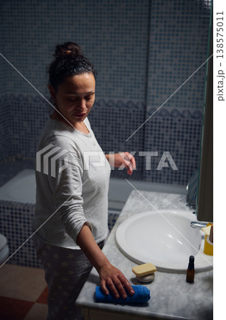 Middle-Aged Woman in Pyjamas Performing Morning Skincare Routine at Bathroom Sink 138575011
