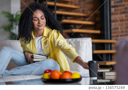Young long-haired woman sitting on sofa with a book while spending her spare time at home Young long-haired woman sitting on sofa with a book while spending her spare time at home 138575289