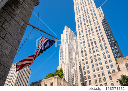 New york, usa august 14,2024. American flag waving before rockefeller center skyscrapers under a clear blue manhattan sky, patriotic urban new york cityscape New york, usa august 14,2024. American flag waving before rockefeller center skyscrapers under a clear blue manhattan sky, patriotic urban new york cityscape 138575382