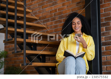 Young woman sitting on the stairs with a book and phone in hands 138575582