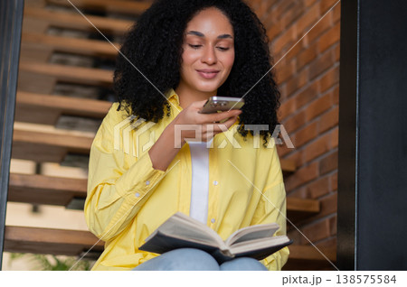Young woman sitting on the stairs with a book and phone in hands 138575584