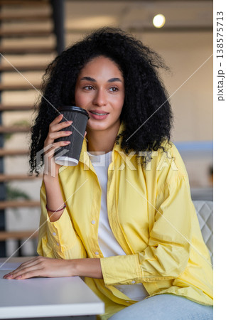 Pretty young brunette woman with coffee in hands looking thoughtful Pretty young brunette woman with coffee in hands looking thoughtful 138575713
