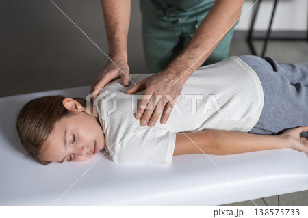 Physiotherapist massaging child spine in medical office Physiotherapist massaging child spine in medical office 138575733