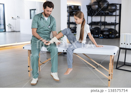 Close up of therapist hands wrapping girl leg 138575754