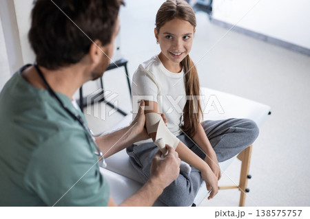 Doctor adjusting elbow support for young patient 138575757