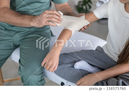 Physiotherapist fixing medical bandage on child elbow 138575760