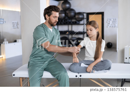 Specialist applying elbow bandage to young girl 138575761