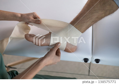 Detail of elastic bandage being wrapped around male patient foot Detail of elastic bandage being wrapped around male patient foot 138575771