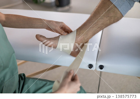 Physiotherapist wrapping elastic bandage on patient ankle Physiotherapist wrapping elastic bandage on patient ankle 138575773
