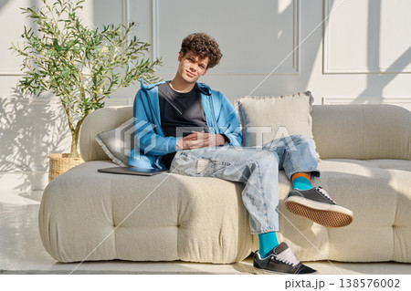 Portrait of handsome young man with curly hair sitting on sofa Portrait of handsome young man with curly hair sitting on sofa 138576002