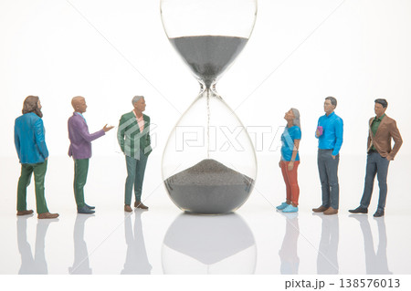 Miniature people gathered around an hourglass with dark sand in a simple setting at a studio 138576013