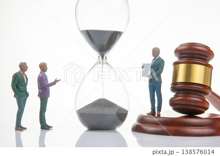 Miniature figurines gather around an hourglass and a gavel during a conversation about time  138576014