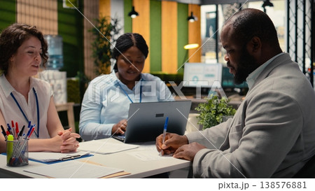 Black male candidate adds signature on employment document for legal terms agreement during HR meeting, finalizing the hiring process and being excited about a new career start. Camera A. 138576881