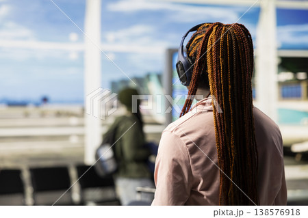African american girl listening to music and waiting for boarding plane, walking around the airport terminal lounge area. Teenager preparing for international flight departure, diverse travelers. African american girl listening to music and waiting for boarding plane, walking around the airport terminal lounge area. Teenager preparing for international flight departure, diverse travelers. 138576918