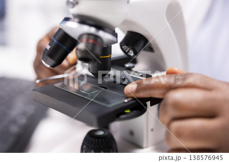 Microscope close up of woman arranging sample tray for experiment in chemistry lab. Detailed investigation of specimen for medical research and nanotechnology, biotechnology solutions. 138576945
