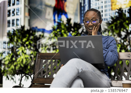 Watching shocking movie, laptop and woman on park bench gasping seeing scene. Having fun, notebook and thrilled young girl in city outdoors surprised by TV show plot twist Watching shocking movie, laptop and woman on park bench gasping seeing scene. Having fun, notebook and thrilled young girl in city outdoors surprised by TV show plot twist 138576947